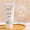 En hvit tube med Green People Fruit Scrub Exfoliator står på et trebrett ved siden av et Dermatologisk testet-ikon.