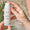 Hender holder en flaske Green People Firming Face & Neck Serum med et Dermatologically Tested-segl over.