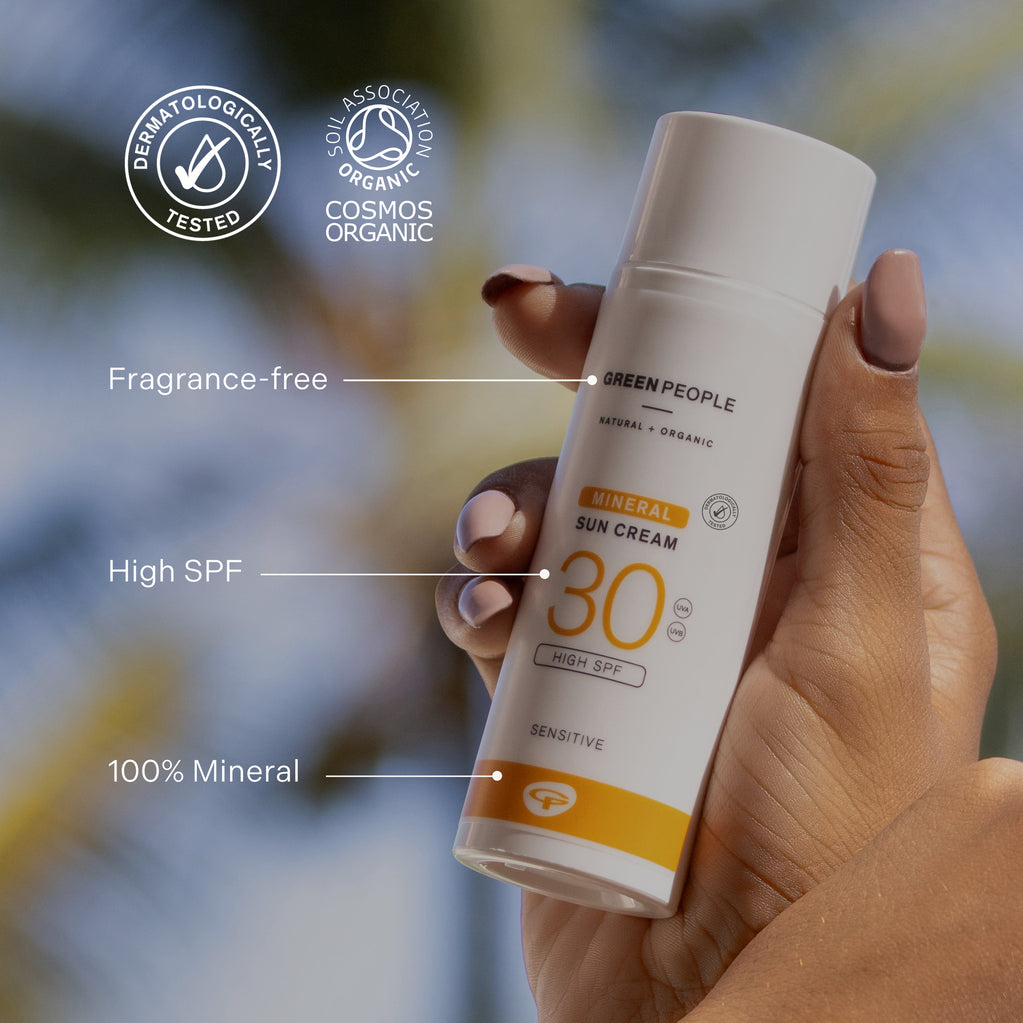 Person som holder en hvit flaske med oransje etikett, viser SPF 30, naturlig, økologisk og dermatologisk testet.