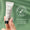 En hånd holder en tube Green People Scent Free Eye Cream 10 ml mot grøn bakgrunn med et «Dermatologisk testet»-ikon.