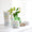 En hvit krukke med Organic Babies Mum & Baby Rescue Balm står på en lys overflate ved siden av en lekemus i tre og en vase med en grønn plante.
