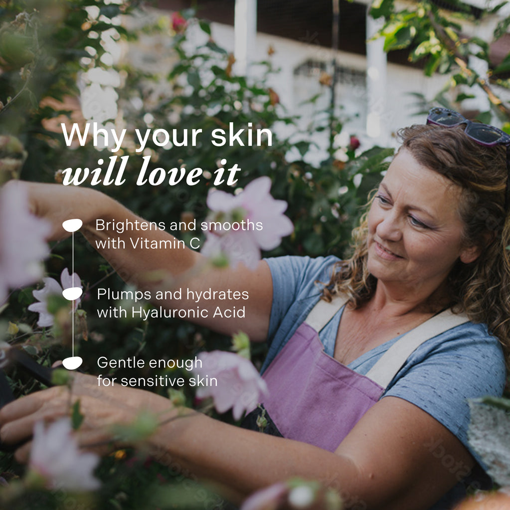A smiling mature woman gardens outdoors near pink flowers, highlighting benefits of Age Defy+ Collagen Boost Vitamin C Serum.
