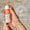 Hender holder en oransje og hvit Oy Clear Skin Cleansing Moisturiser-flaske med et Dermatologisk testet-merke.